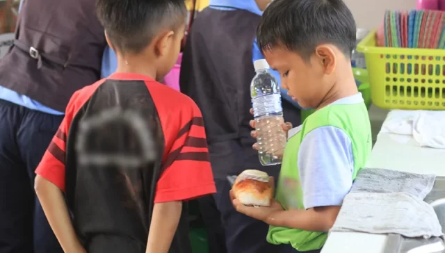 child looking at his bread and holding a bottle of water during school recess.