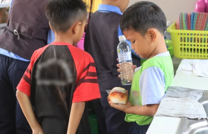 child looking at his bread and holding a bottle of water during school recess.