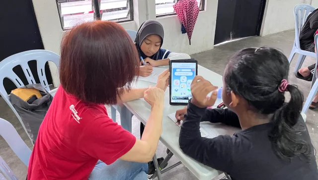 A Malaysian NGO worker interacting with children with a tablet in a 21st century classroom setting.