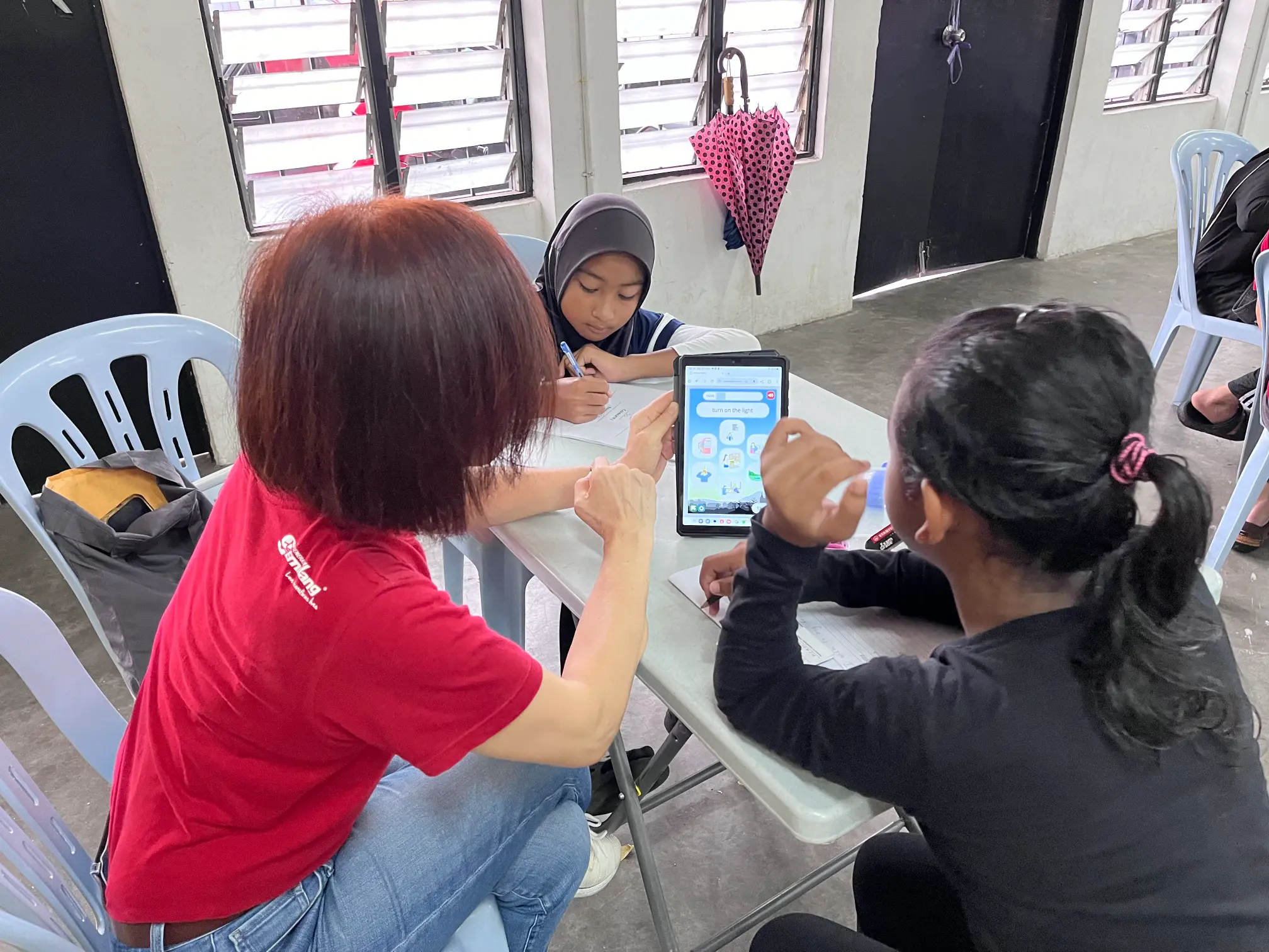 A Malaysian NGO worker interacting with children with a tablet in a 21st century classroom setting.