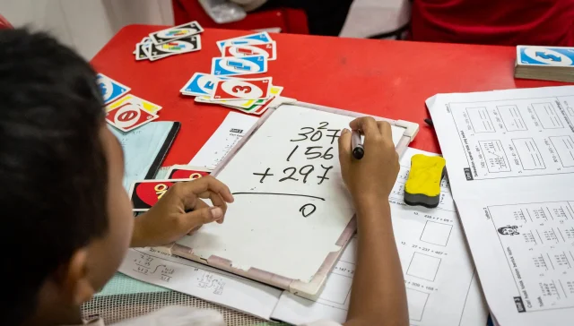 A Malaysian child solving a math equation on a clipboard signifying the education level in Malaysia.