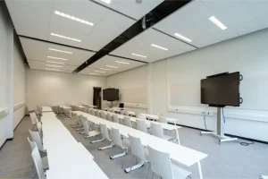 A sleek minimal layout 21st century classroom setting featuring long tables, open space and TV screens.