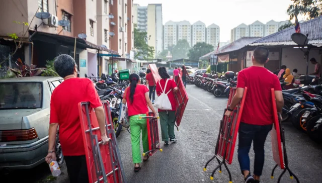 A group of Malaysian charity volunteers in red uniforms carrying tables signifying why charity is important.