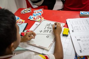 seorang budak lelaki menulis nombor matematik atas papan putih kecil sebagai aktiviti sukarelawan.