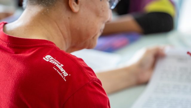 seorang lelaki tua membuat aktiviti sukarelawan memakai baju merah dengan lambang generasi gemilang.