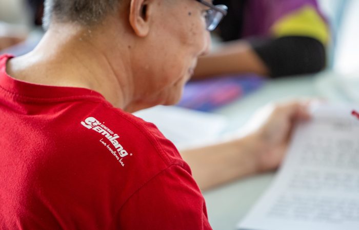 seorang lelaki tua membuat aktiviti sukarelawan memakai baju merah dengan lambang generasi gemilang.