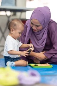 A mother wearing a purple hijab and her young son playing together to show what is early childhood education about